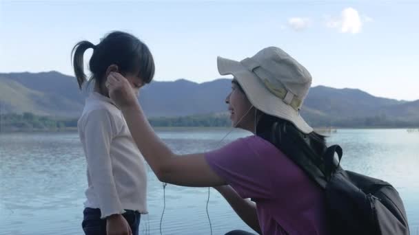 어머니와 아름다운 호수의 배경에서 스마트폰으로 음악을 듣는다 가정생활 — 비디오