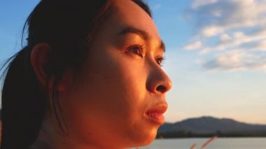 Umut dolu bir kadının, gün batımındaki göl kıyısındaki suya bakışını yakından çek..