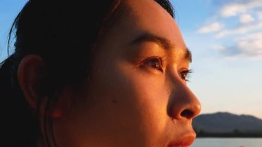 Umut dolu bir kadının, gün batımındaki göl kıyısındaki suya bakışını yakından çek..