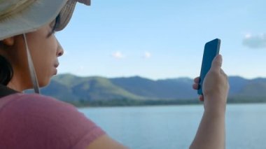 Genç bayan turistler güzel günbatımı gölü arka planında akıllı telefonlardan sohbet ediyorlar. Yaşam tarzı ve Tatil kavramları.