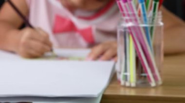 Şirin küçük bir kız evdeki masada renkli kalemlerle kağıda gökkuşağı çiziyor..