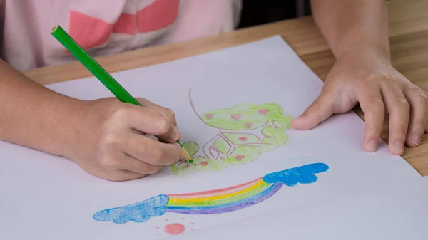 自宅のテーブルで色鉛筆で虹と木を描く子供の手を閉じる — ストック写真