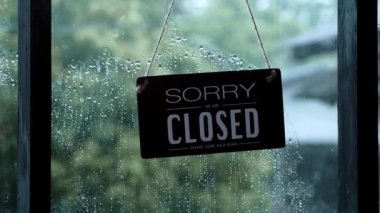 An open sign hanging on the front door of the restaurant swaying on a rainy day.