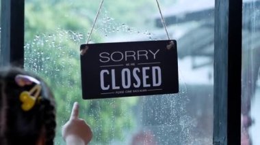An open sign hanging on the front door of the restaurant swaying on a rainy day.