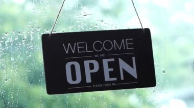 An open sign hanging on the front door of the restaurant swaying on a rainy day.