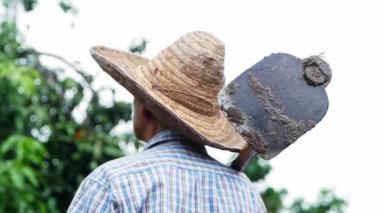 Old farmers in a straw hat held a hoe across his shoulder and facing the sky, waiting for the seasonal rain. Rural agriculture concept.