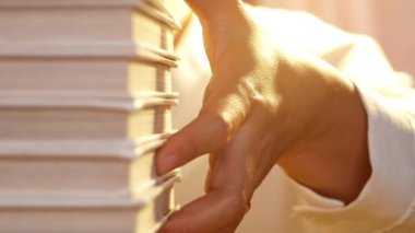 Yakın plan genç kadının eli evdeki masadaki kitap yığınından bir kitap seçiyor. Evde kalıp koronavirüs salgınını karantinaya alın..