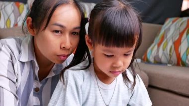 Mutlu anne ve kızları oturma odasındaki dizüstü bilgisayardan resim yapmayı öğrendiler. Annem, kızların kağıda resim çizmelerine yardım ediyor. Ev okulu konsepti. Anaokulu çevrimiçi dersleri.