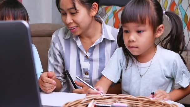 快乐的母亲和女儿们学会了在客厅里通过笔记本电脑画画 妈妈帮助女孩们在纸上画一幅画 家庭学校概念 幼稚园网上课程 — 图库视频影像