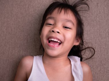 Oturma odasındaki kanepede uzanmış, kameraya bakıyor ve evde oynarken gülümsüyor..