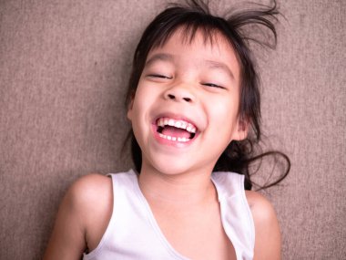 Oturma odasındaki kanepede uzanmış, kameraya bakıyor ve evde oynarken gülümsüyor..