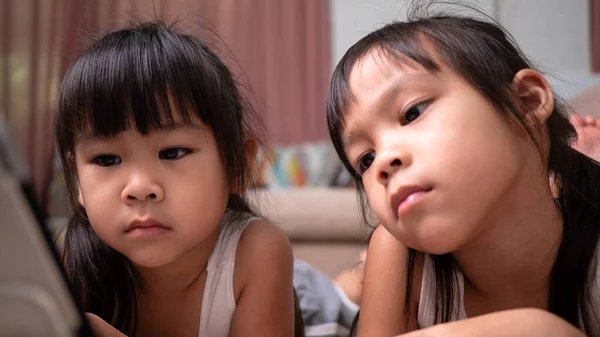 Duas Meninas Irmãs Deitadas Sofá Assistindo Tablets Digitais Juntas Sala — Fotografia de Stock