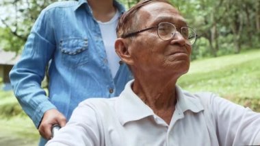 Büyükbabanın omzunu parkta tekerlekli sandalyede tutan torunun yakın çekimi. Tatilde aile hayatı.