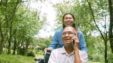Torunu parkta tekerlekli sandalye iterken neşeli engelli bir adam akıllı telefondan konuşuyor. Tatilde aile hayatı.