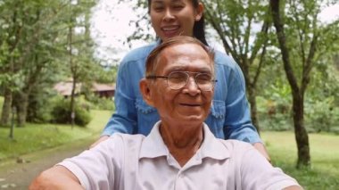 Büyükbabam tekerlekli sandalyede torunuyla parkta doğanın tadını çıkarıyor. Tatilde aile hayatı.