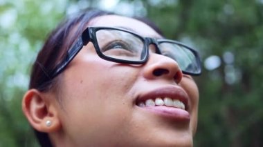 Gözlüklü, gülen yüzlü, ilkbahar bahçesinde doğanın ortasında duran kadının yüzünü kapat. Seyahat ve mutluluk kavramları.