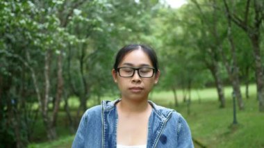 Bahar bahçesinde doğanın ortasında duran gülen yüzlü kameraya bakan gözlüklü bir kadının portresi. Seyahat ve mutluluk kavramları.