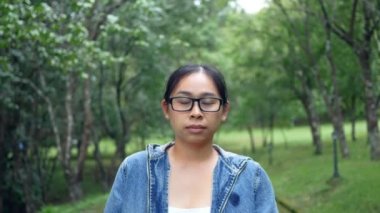 Bahar bahçesinde doğanın ortasında duran gülen yüzlü kameraya bakan gözlüklü bir kadının portresi. Seyahat ve mutluluk kavramları.