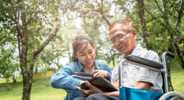 Büyükbaba tekerlekli sandalyede ve torun parkta dijital tabletle eğleniyor. Tatilde aile hayatı.