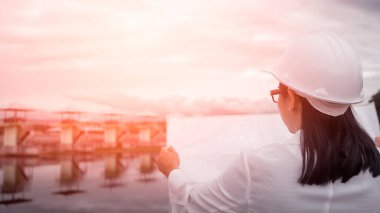 Beyaz kasklı, konuşan bir telsiz iletişimi (walkie talkie) ve hidroelektrik barajında çalışan kadın mühendis. Temiz enerji ve su yönetimi kavramları.