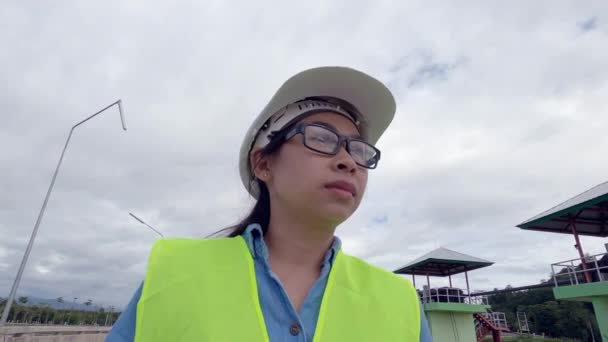 身穿白色头盔和黄色制服的女工程师拿着一个蓝图 环视大坝的建筑工地 以发电 — 图库视频影像