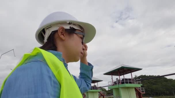 身穿白色头盔和黄色制服的女工程师拿着一个蓝图 环视大坝的建筑工地 以发电 — 图库视频影像