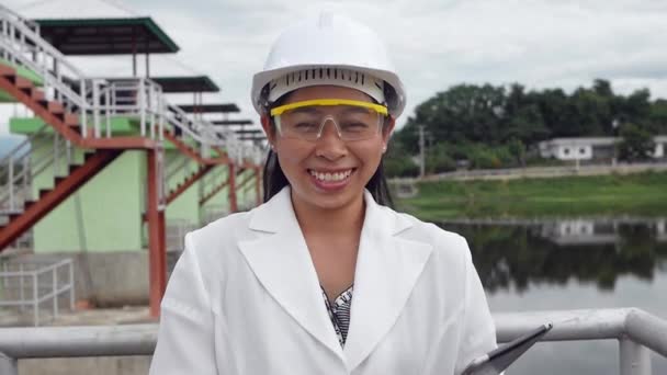 戴头盔的女工程师一边拿着一块数字平板电脑在大坝工地发电 一边微笑着看着摄像机 — 图库视频影像