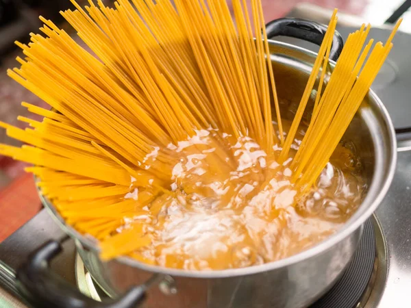Çiğ spagetti, mutfak kabında kaynar suda pişiriliyor. Sağlıklı İtalyan Yemek ve Pişirme kavramları.