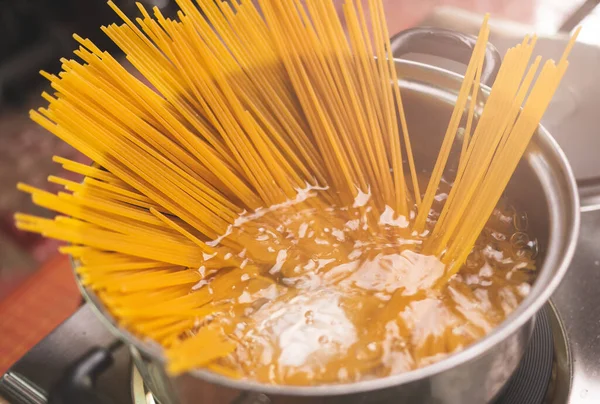 Çiğ spagetti, mutfak kabında kaynar suda pişiriliyor. Sağlıklı İtalyan Yemek ve Pişirme kavramları.