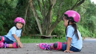 Koruyucu pedler ve kaskla parkta paten yapmaya çalışan iki kardeş kardeş. Çocuklar için aktif açık hava sporu.