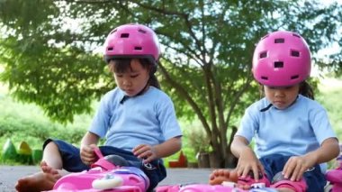Genç anne, park yolundaki paten antrenmanından önce kızının koruyucu pedleri ve kaskını takmasına yardım ediyor. Çocuklar için aktif açık hava sporu.