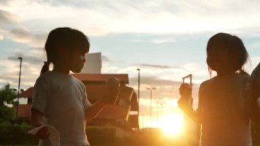 İki kardeş gün batımında dışarıda tatlı tatlı dondurma yiyorlar. İki mutlu genç çocuk parkta tatil yaparken tatlının tadını çıkarıyor..