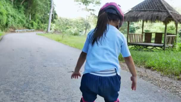 夏の公園でローラースケートに保護パッドと安全ヘルメットの学習を身に着けている女の子 子供のためのアクティブな屋外スポーツ — ストック動画