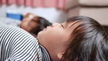 Küçük tatlı kızlar yoga pozu veriyorlar. Küçük çocuklar evlerinde mavi yoga minderi üzerinde egzersiz yapıyorlar. Mutlu Asyalı kız kardeşler tatilde birlikte vakit geçiriyorlar..