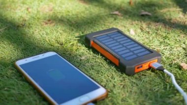 Çimlerin üzerinde güneş panelleri olan şarj edilebilir mobil güç paketi. Cep telefonu, tablet ya da akıllı telefona bağlanıp şarj ediliyor. USB şarjlı güneş yastığı.