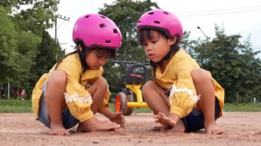 Kasklı iki küçük kız kardeş güneşli bir yaz gününde parkta kumla oynuyorlar, bisiklet antrenmanından sonra mola veriyorlar. hayal gücünü ve keşfi geliştir.