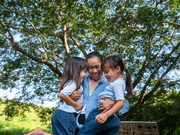 庭で暖かく晴れた夏の日にお母さんが笑って抱き合っている2人の兄弟の小さな女の子 若いです女の子とともに彼女の母親支出日で公園 — ストック写真