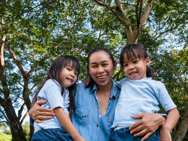 庭で暖かく晴れた夏の日にお母さんが笑って抱き合っている2人の兄弟の小さな女の子 若いです女の子とともに彼女の母親支出日で公園 — ストック写真