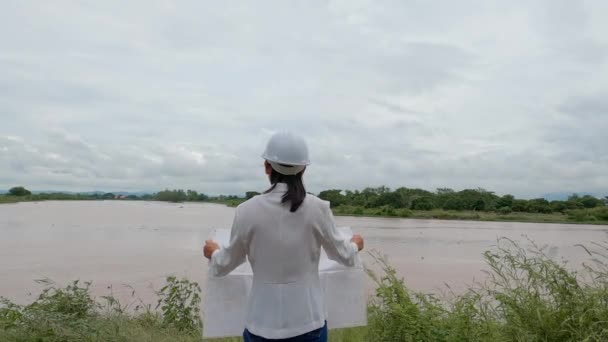 Женщина Инженер Держащая Руках Чертеж Прогуливается Вокруг Плотины Электрификации Реки — стоковое видео