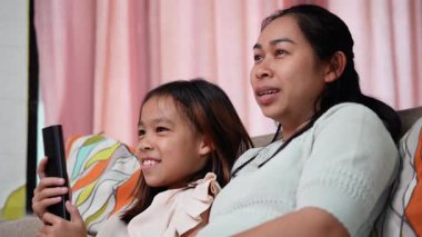 Mutlu Asyalı anne ve iki kızı evde birlikte otururken heyecanla gülümsüyor ve ellerini kaldırıyorlar.. 