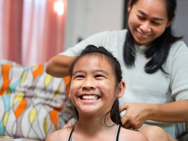 Bir annenin kızının saçını ördüğü sıcak ve samimi bir an. Küçük kız evinde gülümserken..