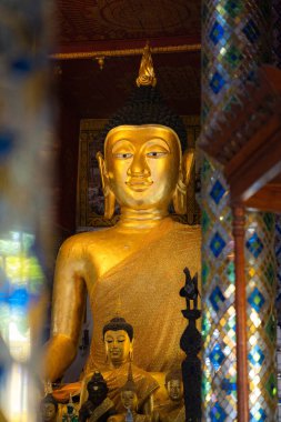 Tayland tapınağındaki altın Buda heykeli Budizm, inanç, barış ve geleneksel Tayland kültürünü temsil eden küçük Buda resimleriyle çevrili..