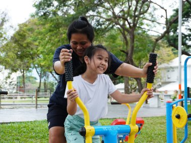 Parlak renkli spor aletleriyle parkta eglenceli bir egzersiz yapan bir anne ve kiz. Aile sağlığı, sağlık ve toplum ortamında ortak egzersizin keyfi.