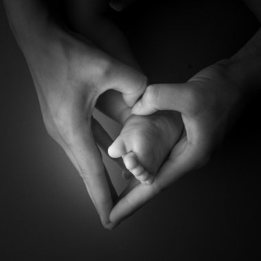 Yeni doğan bebek bacakları gri arka plan üzerinde izole anne el ile