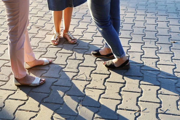 Feet of women in sandals stand in circle on paving slabs on summer sunny day with copy space