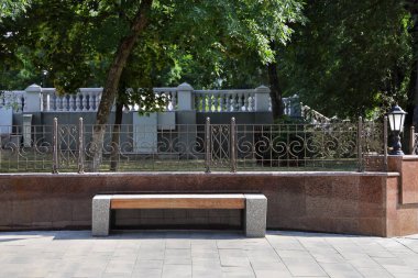 Yaz günü kamu parkının yanındaki duvarın yanındaki bankta dekoratif çitlerle.