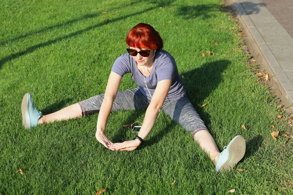 Spor Kıyafetli Genç Kızıl Saçlı Kadın Çimenlerde Oturur Güneşli Bir — Stok fotoğraf
