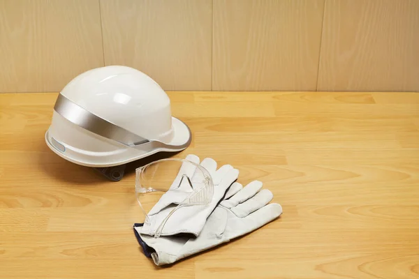 White construction helmet, safety goggles and leather gloves on table with copy space