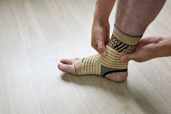 Human hands fix an elastic bandage sock to protect the ankle of the leg from sprains, close-up