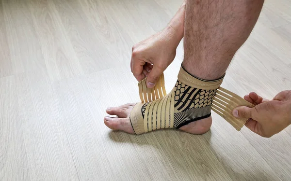 Human hands fix an elastic bandage sock to protect the ankle of the leg from sprains, close-up
